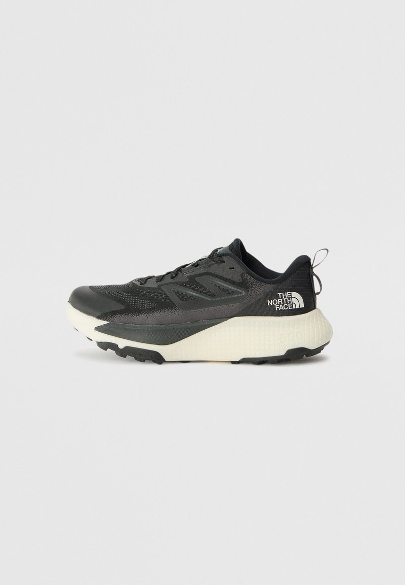 Black athletic shoe with a textured upper, featuring gray accents and a white midsole. Includes a pull tab and prominent brand logo on the heel.