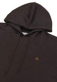 Podroben posnetek temno rjave kapuce z vrvicami in majhnim kvadratnim logotipom na prsih, na belem ozadju.