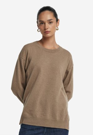 Sweater beige oversize en tissu doux, avec un col rond, des épaules tombantes et des détails en côtes à l'ourlet.