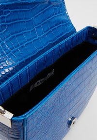 Borsa a tracolla blu con motivo coccodrillo, texture lucida, hardware argentato e interno nero con etichetta del marchio.