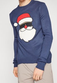 Blauer Strickpullover mit großem Weihnachtsmann-Gesicht, roter Mütze, Sonnenbrille und flauschigem weißen Bart. Mit gerippten Bündchen und Saum.