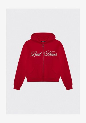 Czerwona rozpinana bluza z kapturem na sznurki, kangurzymi kieszeniami oraz białym haftowanym napisem "Lokalni Bohaterowie" z przodu. Miękki materiał.