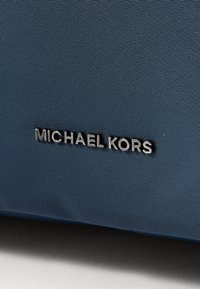 Plava najlonska torba s teksturiranom površinom i srebrnim logotipom "Michael Kors" sprijeda kao oznakom branda.
