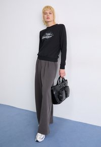 Sweat à capuche noir avec graphique "Nike Sportswear", pantalon plissé gris, baskets argentées et sac fourre-tout en cuir noir.