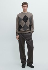 Brauner gestrickter Pullover mit Rautenmuster in Grau und Schwarz, kombiniert mit dunkler Hose. Die Textur wirkt weich und der Stoff sieht leicht aus.