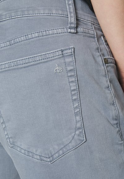 Light blue denim jeans featuring a back pocket with subtle stitching and a small embroidered logo. Smooth texture, close-fit design.