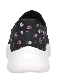 Zapatilla negra tipo slip-on con pequeño patrón floral en rosa, blanco y naranja en el talón y suela blanca texturizada.