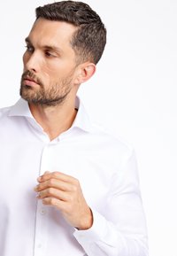 Witte button-up overhemd met een spread collar, met een gladde textuur en een getailleerd ontwerp, gedragen door een persoon met kort, gestyled haar.