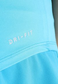 Primer plano de una tela azul claro con el texto blanco "DRI-FIT" y costuras dobles visibles en un material de ropa deportiva.