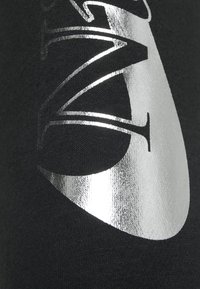 Svart tyg med ett silverreflekterande tryck med en stiliserad design. Texturen är slät, med en subtil glans på det tryckta området.