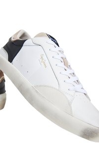 Vita och svarta sneakers i läder och mesh. Funktioner inkluderar snörning, guldlogo och en texturerad tåhätta. Sulan visar lätt slitage.