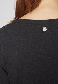 Camicia di tessuto grigio scuro con scollatura rotonda e un bottone decorativo in argento sul retro. Texture liscia e design casual.