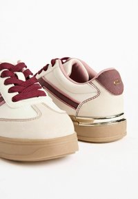 Kreemivärvilised sneakersid, millel on maroonid aktsendid ja tekstureeritud viimistlus. Omab pruuni tallat ja metallilist detaile kanna piirkonnas.