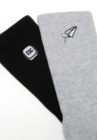 Schwarze und graue Baumwollsocken mit gerippter Textur. Die schwarze Socke hat eine gestickte "ESC"-Taste; die graue Socke hat ein Papierflugzeug-Muster.