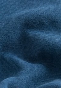 Sininen neulottu kangas, jossa on sileä pinta, esittelee tasaisen kuvion ja hienovaraisia sävyvaihteluita, jotka korostavat sen pehmeää laskeutumista.