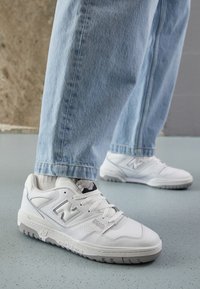Vita New Balance 550-sneakers har en slät läderöverdel, perforerade sidodetaljer och en texturerad gummisula. Bärs tillsammans med ljusblå denim.