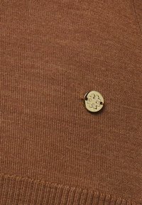 Ruskea neulottu kangas, jossa on pyöreä kultainen korostuspainike, jossa on kukkakuvio ja kaksi kiinnitysreikää. Tasainen rakenne ja tasainen ompelu.