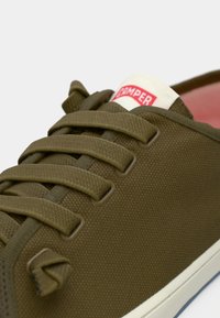 Baskets en toile vert olive avec des lacets plats, une finition texturée et une languette crème ornée d'un logo rouge "Camper".