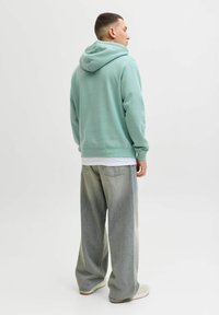 Miętowa bluza z kapturem z troczkami, o luźnym kroju, zestawiona z jasnoszarymi, szerokimi spodniami dżinsowymi. Gładka faktura, minimalistyczne logo.