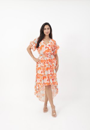 Robe portefeuille florale orange avec des accents bleus et blancs, présentant des manches flottantes, une taille cintrée et un ourlet asymétrique. Talons transparents.