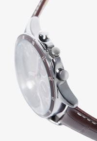 Reloj cronógrafo con caja de acero inoxidable plateado, correa de cuero marrón, esfera clara y tres pulsadores en el lado derecho para funcionalidad.