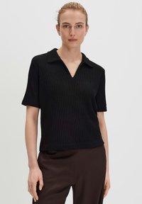 Zwarte geribbelde polo met korte mouwen, een V-hals en gestructureerde kraag, gemaakt van een zachte, textuurrijke brei-stof.