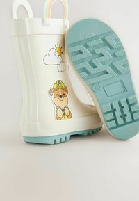 Botte de pluie en caoutchouc blanc avec une semelle bleue et une texture antidérapante. Présente un design de chien de dessin animé et de nuage, avec une poignée bicolore.