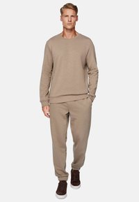 Beige sweatshirt with a round neckline and ribbed cuffs, paired with matching tapered sweatpants and brown suede sneakers.