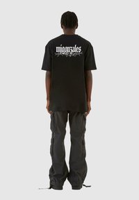 Svart oversized t-skjorte med hvit grafisk tekst på baksiden, kombinert med mørke cargo-bukser. Stoffet ser mykt ut med en avslappet passform.