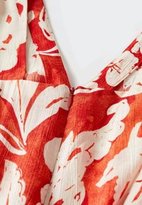 Červená a bílá látka s květinovým vzorem a texturovaným povrchem, s výstřihem do V a malým zipem uprostřed.