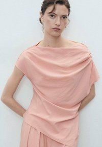 Haut drapé rose doux avec un large décolleté bateau. Fabriqué à partir d'un tissu léger, il présente des manches courtes et une silhouette décontractée.