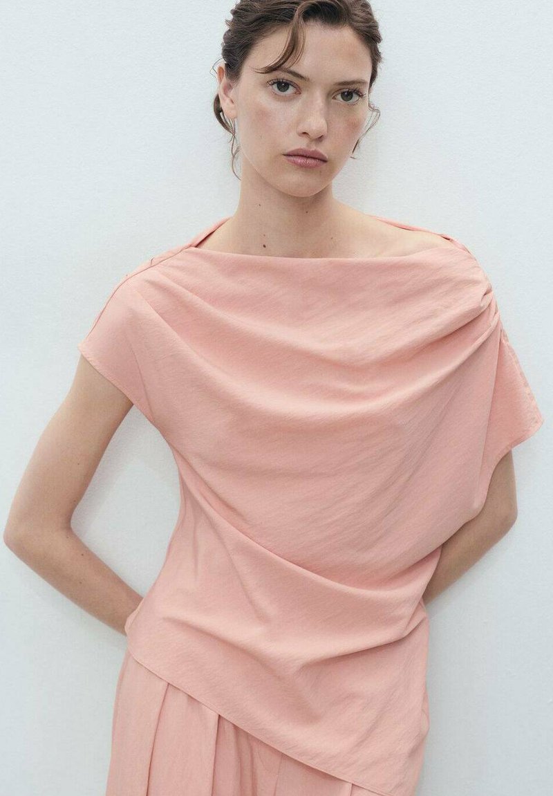 Haut drapé rose doux avec un large décolleté bateau. Fabriqué à partir d'un tissu léger, il présente des manches courtes et une silhouette décontractée.