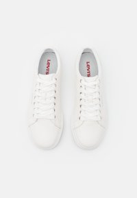 Sneaker bianchi in pelle con una superficie liscia, dotati di lacci piatti, punta rotonda e un interno grigio con branding rosso.