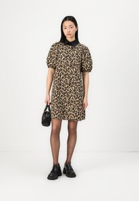 Rochie cu imprimeu de leopard, cu guler negru și mâneci scurte tip puff. Asortată cu o geantă mică neagră și pantofi masivi negri. Textură netedă.