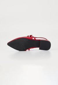 Scarpa con tacco in pelle rossa, punta affusolata, sottili lacci e suola in gomma nera testurizzata, con tacco a blocco basso.