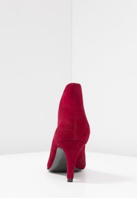 Zapato de tacón alto de ante rojo con punta afilada y un tacón delgado y resistente. Textura suave con detalles de costura mínimos visibles.