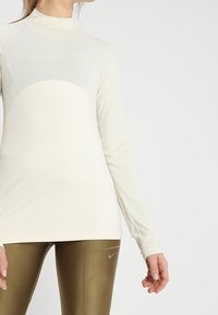 Długi rękaw sportowy top w kolorze off-white z teksturowanym paskowanym wzorem, z wysokim kołnierzem i dopasowanym krojem.