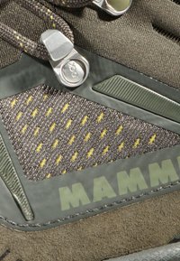 Buty trekkingowe z szarym materiałowym wierzchem i żółtymi akcentami, gumowymi panelami oraz wyraźnym logo marki. Zawierają metalowy detal z blokadą sznurowadeł.
