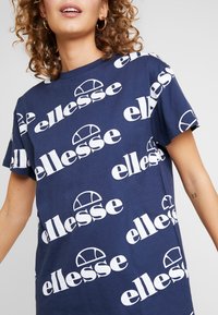 Navy blue cotton t-shirt featuring repeated white "ellesse" logo in various orientations. Short sleeves, relaxed fit, no additional embellishments.