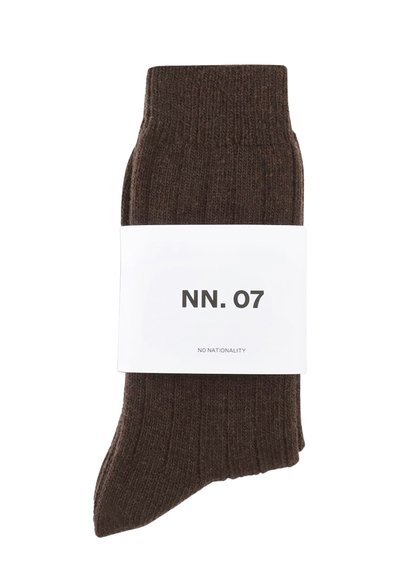 Brązowe skarpetki w prążki o miękkiej teksturze, zapakowane z białą etykietą z napisem "NN. 07" i "NO NATIONALITY" w czarnym kolorze.