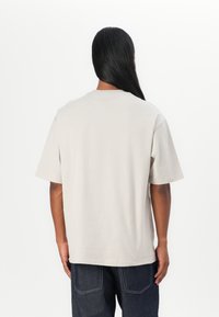 Beige bomuld t-shirt med korte ærmer og rund hals, med en afslappet pasform og glat tekstur, vist fra ryggen.