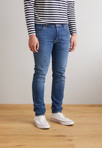 Slim-fit blue jeans made of denim, featuring a faded look. Paired with white sneakers and a horizontally striped long-sleeve shirt.
