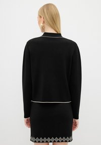 Svart stickad tröja med en kortad design, med långa ärmar och en krämfärgad kant nertill, tillsammans med en kjol prydd med ett diamantmönster.