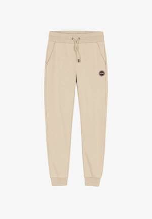 Pantaloni della tuta beige realizzati in morbido tessuto, con vita elasticizzata e cordoncino, tasche laterali e un'etichetta rotonda con logo.