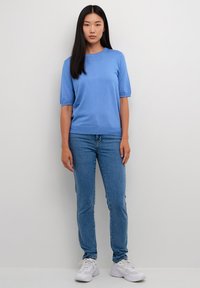 Lichtblauwe trui met korte mouwen en ronde hals, gecombineerd met middelblauwe, nauwsluitende jeans en witte sneakers. Gladde textuur, casual pasvorm.