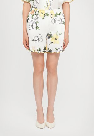 Pantaloni corti bianchi a fiori con ricami di fiori gialli, arancioni e verdi. Presentano un bordo ondulato e una vita elastica con cordino.