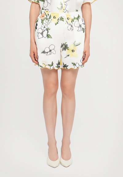 Hvide blomstrede shorts med broderede blomster i gul, orange og grøn. Har en scalloperet kant og elastisk talje med snøre.