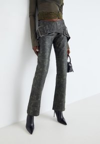 Svarta läderbyxor med en urblekt grön finish, med ett brett bälte med nitar, och accentuerade av en åtsittande olivgrön topp och spetsiga stiletto-klackar.