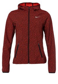 Veste à capuche rouge et noire à motif, avec fermeture éclair intégrale à l’avant, poches latérales zippées et petit logo Nike blanc sur la partie supérieure gauche de la poitrine.