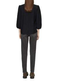 Schwarzes Oberteil mit Puffärmeln, kombiniert mit grauen Slim-Fit-Jeans. Das Oberteil hat eine weiche Textur, während die Jeans feine Details an den Gesäßtaschen aufweisen.